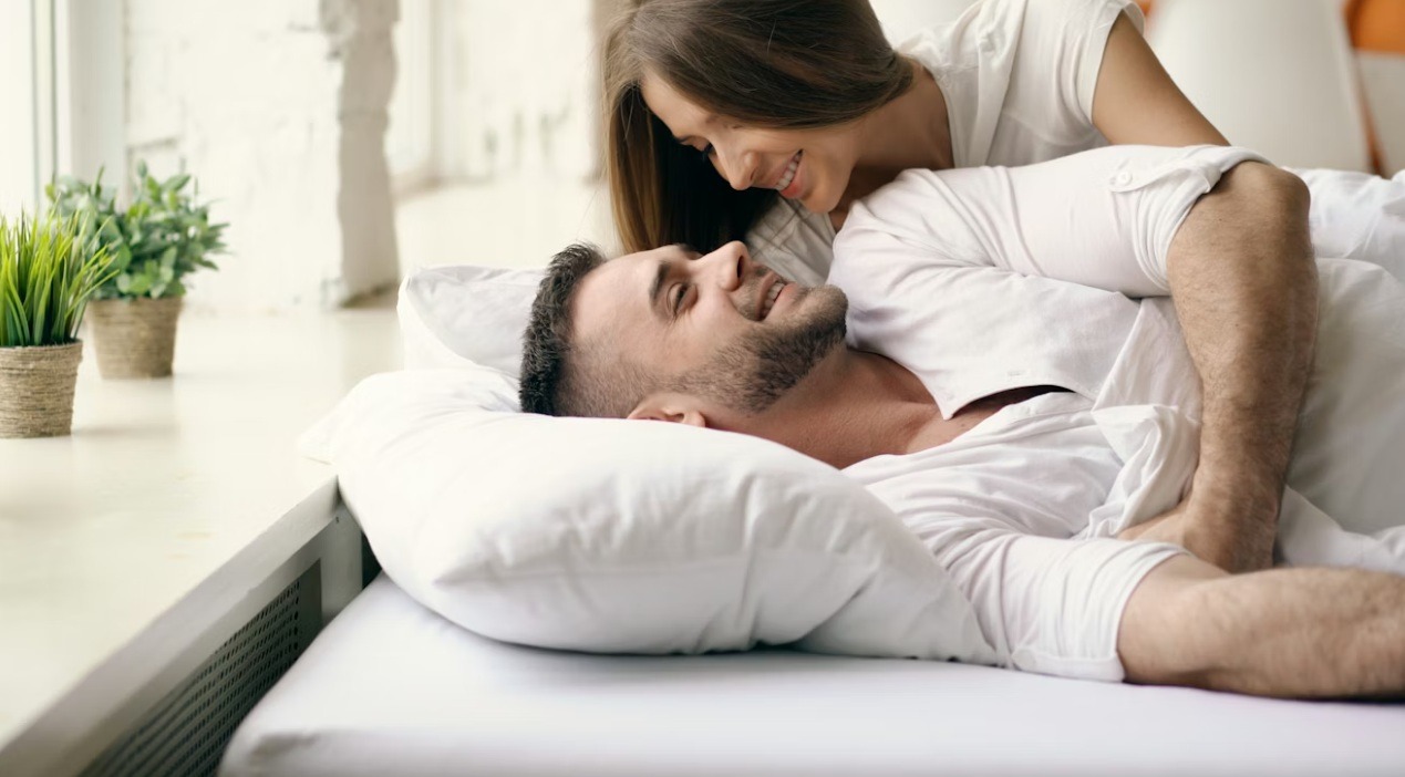 Mladi par leži zagrljen u krevetu u nežnoj intimnoj atmosferi, ilustrujući peting i emotivnu bliskost